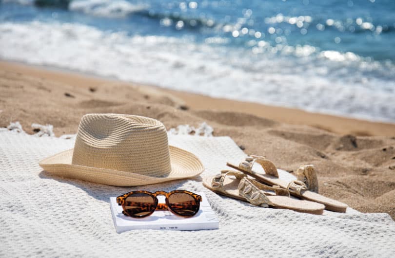 תמונה של כובע, משקפיים וסנדלים על חוף הים